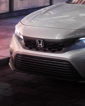 Vista frontal del Honda Civic Sedán Touring 2024 en Lunar Silver Metallic estacionado en una calle de la ciudad por la noche (sedán compacto).