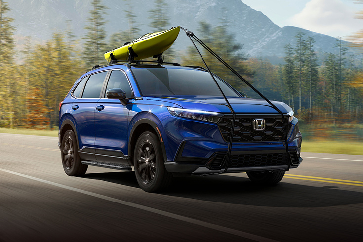 Vista frontal de la Honda CR-V Sport Touring Hybrid 2025 en Canyon River Blue Metallic circulando con un kayak (SUV crossover compacta).