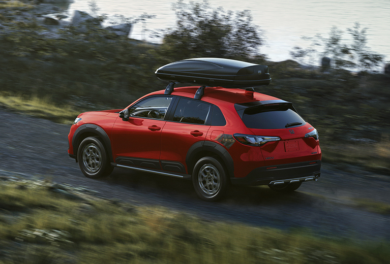 Vista trasera de la HR-V 2026 en rojo con accesorios originales de Honda que conduce por una carretera rural
